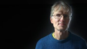 Thomas Gustafsson tittar in i kameran och står mot en svart bakgrund