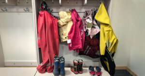 Rosa regnkläder, gul jacka, gummistövlar och några skor vid barnens platser på sommarförskolan.