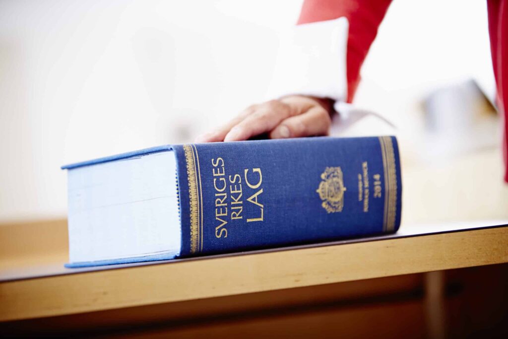 Någon håller sin ena hand på en igenslagen lagbok över Sveriges rikes lag. Lagen reglerar vilka som ska utses till förvaltare och gode män.