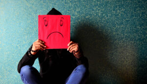 Pojke som sitter med benen i kors mot en grön bakgrund. Framför sig har han ett rött paper med en smiley som visar en ledsen gubbe. Foto: PDPics, Pixabay