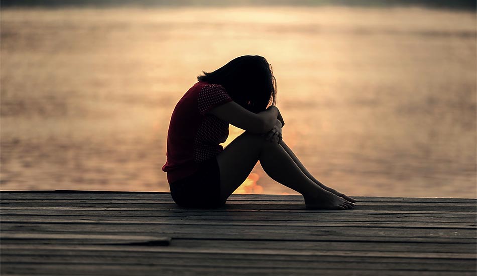 Flicka som sitter hopkrupen i sorg på en brygga vid vatten. Foto: Pexels-Pixabay