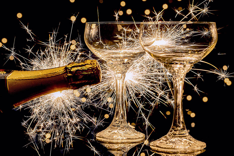 Två glas som skålar och en champagneflaska som sprutar ut sitt innehåll. Guldglittrigt mot svart bakgrund. Foto: Myriams Fotos, Pixabay