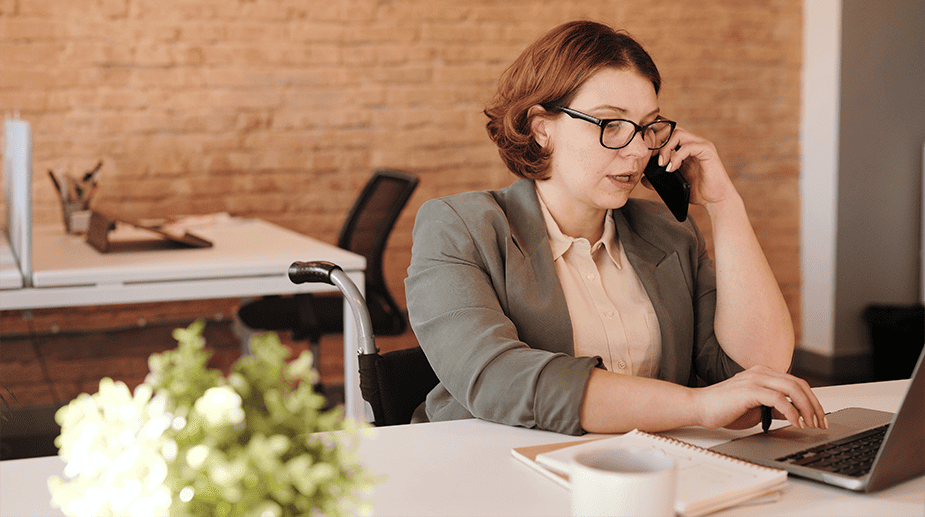Kvinna som talar i telefon. Hon sitter vid ett skrivbord och har en laptop framför sig. Foto: Marcus Aurelius från Pexels