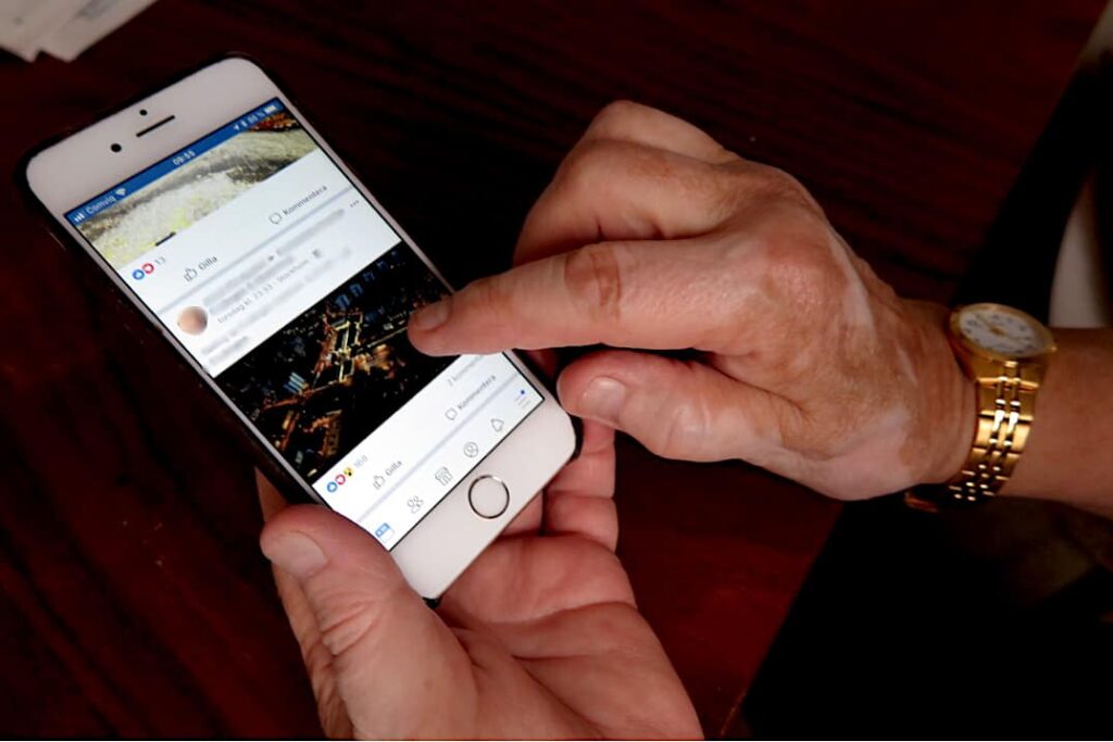 Äldre kvinnas hand som scrollar på mobiltelefon.