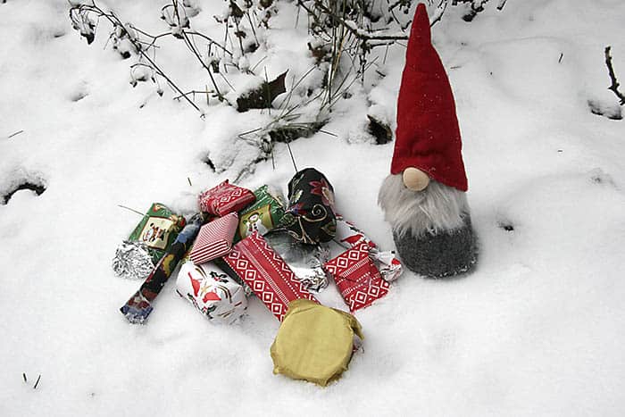 Tomte med julklappar som står i snö. Trädgrenar i bakgrunden. Foto: Monica Atterberg