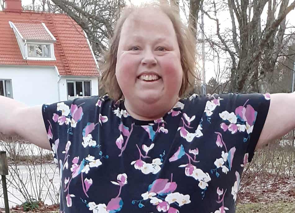 Marina Sängängel, ljushårig kvinna, halvporträtt, blåblommig blus. I bakgrunden hus med rött tegeltak..