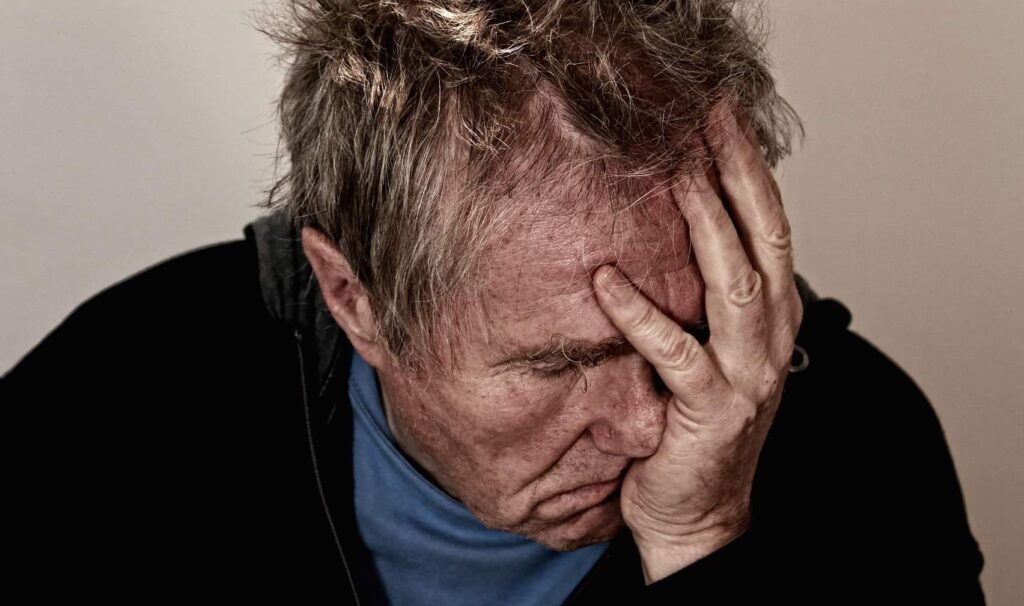 Utmattad man med ansiktet i handen beskuren