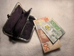 Tom svart portmonnä med två sedlar vid sidan om, 200 och 50 kronor mot vit bakgrund.