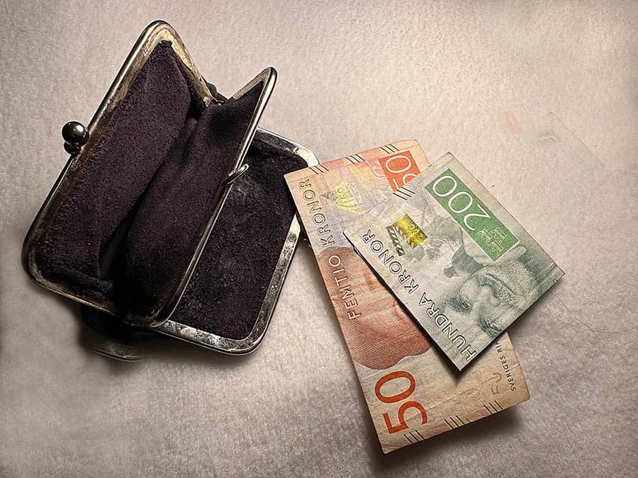 Tom svart portmonnä med två sedlar vid sidan om, 200 och 50 kronor mot vit bakgrund.