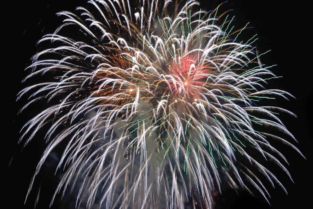 Vitt fyrverkeri med rött i mitten mot svart bakgrund.