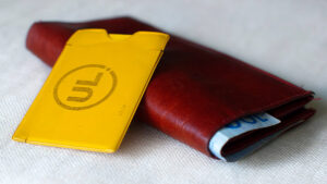 På bilden syns ett gult inplastat resekort som gäller för resor i kollektivtrafiken i Uppsala län. Den ligger ovanpå en vinröd plånbok med sedlar i. Foto Tua Lilja