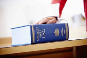 Någon håller sin ena hand på en igenslagen lagbok över Sveriges rikes lag. Lagen reglerar vilka som ska utses till förvaltare och gode män.