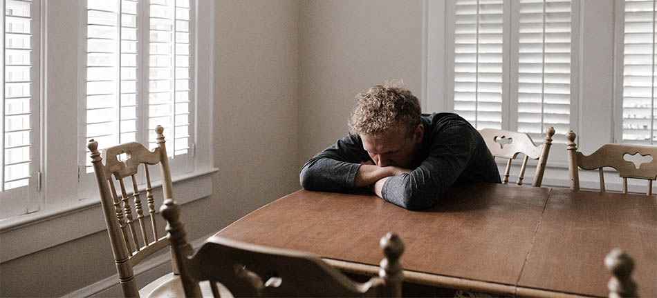 Deprimerad man med armarna i kors vid ett bord inomhus. Foto: Andrew Neel. Pexels