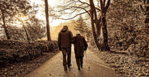 Ett äldre par, sedda bakifrån, som promenerar i en skogsglänta. Foto: Mabel Amber från Pixabay