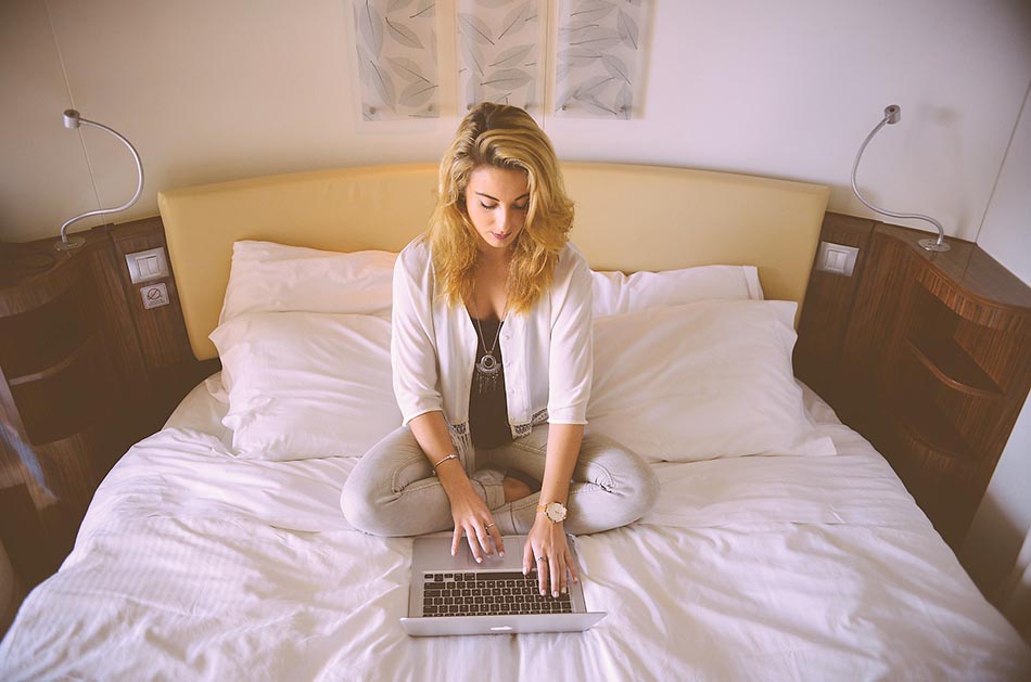 Ung kvinna med sin laptop i sängen i sovrummet. Foto: Stokpic från Pixabay