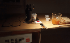 Nattduksbord nattetid på ett sjukhus. På bordet finns bland annat en smörgås i plast, ett glas juice, en medicinburk och ett par glasögon. Foto: Ann Qvarnström