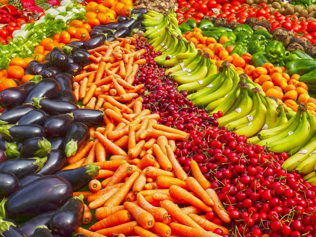 Hela bilden består av olika färgglada frukter och grönsaker: tomater, gröna paprikor, morötter, auberginer, apelsiner, körsbär med flera.