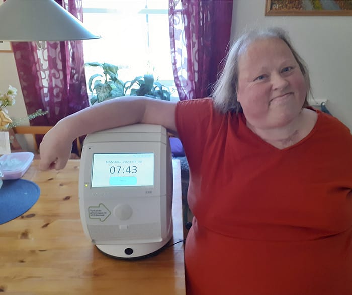 Marina Sångängel i röd klänning står i sitt hem med sin apodosrobot.
